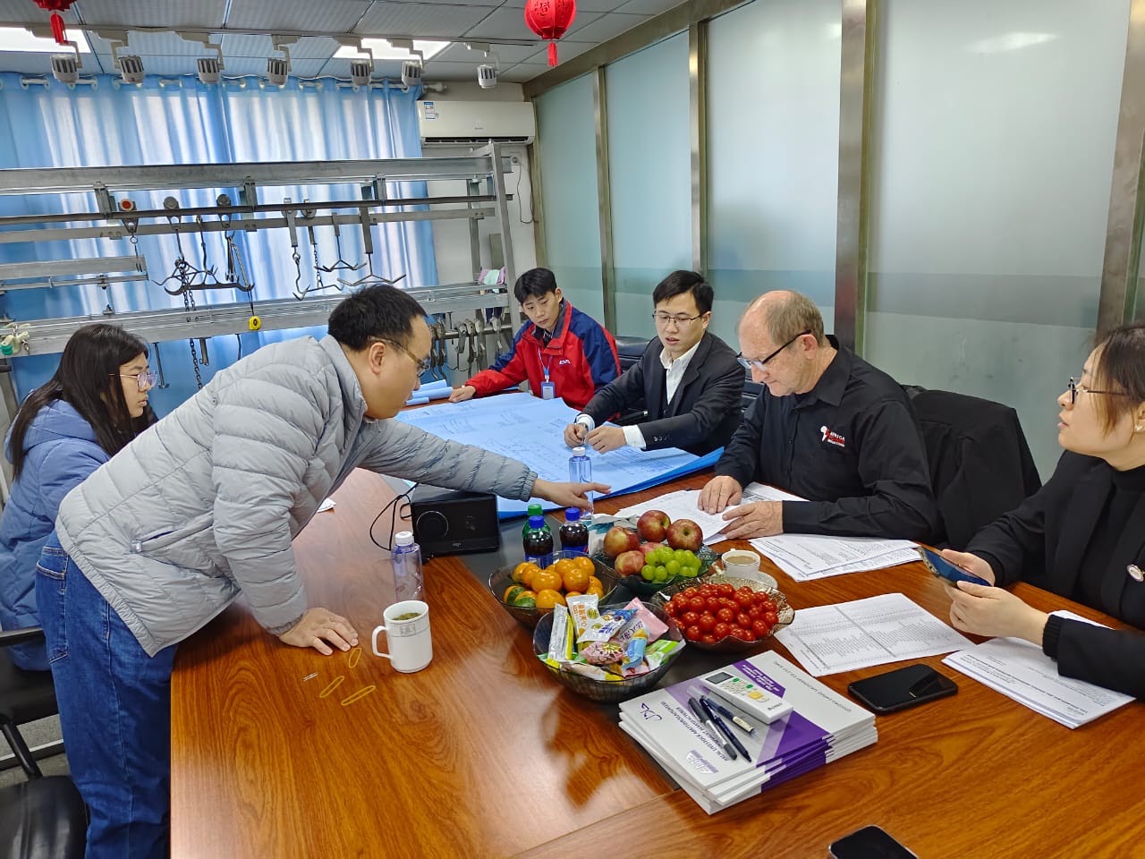 Chris Peo reviewing technical drawings around a table with a Chinese supplier team
